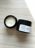 Lip scrub in an amber glass jar with a black plastic lid on a wooden surface